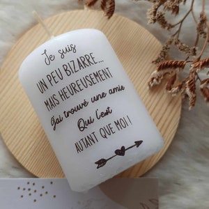 Peut inclure: Bougie blanche avec un motif de flèche et de cœur brun. La bougie porte le texte "Je suis un peu bizarre... mais heureusement j'ai trouvé une amie qui l'est autant que moi!"