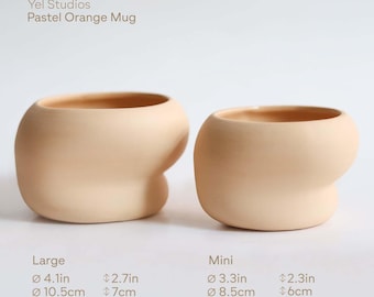 Puede incluir: Dos tazas de color naranja pastel, una grande y otra mini, con formas redondeadas y orgánicas. La taza grande tiene 10,5 cm de diámetro y 7 cm de ancho, mientras que la mini tiene 8,5 cm de diámetro y 6 cm de ancho. El texto "Yel Studios Pastel Orange Mug" está arriba.