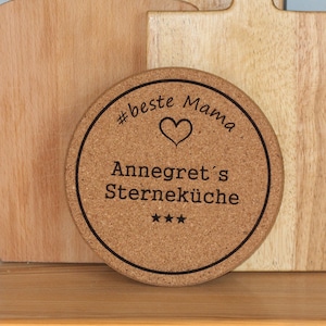 Könnte beinhalten: Ein runder Korkuntersetzer mit schwarzem Rand und dem Text "#beste Mama" mit einem Herzsymbol, "Annegret's Sterneküche" und drei Sternen.