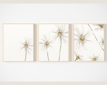 May include: A set of three framed watercolor prints featuring white daisies with yellow centers on a white background.
