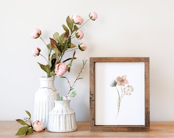 May include: A framed floral print with a watercolor design of delicate flowers in shades of pink and brown. Two white ceramic vases with pink flowers and greenery are on a wooden surface.