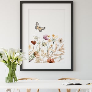 May include: A framed watercolor print featuring a butterfly and a variety of wildflowers in shades of pink, brown, and yellow. The print is set against a white background.