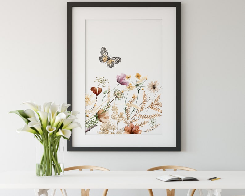 May include: A framed watercolor print featuring a butterfly and a variety of wildflowers in shades of pink, brown, and yellow. The print is set against a white background.