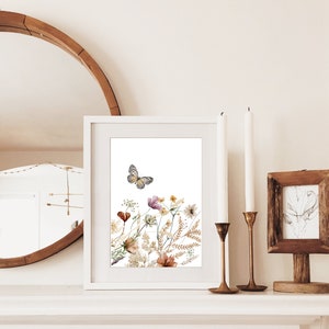 May include: A white framed print with a watercolor illustration of a butterfly flying over a bouquet of dried flowers in shades of brown, yellow, and pink.