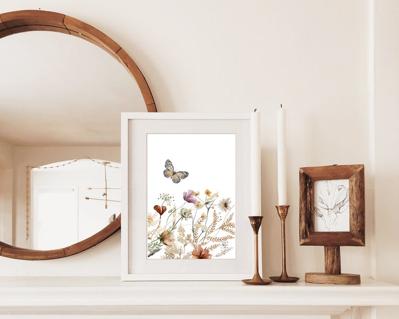 May include: A white framed print with a watercolor illustration of a butterfly flying over a bouquet of dried flowers in shades of brown, yellow, and pink.