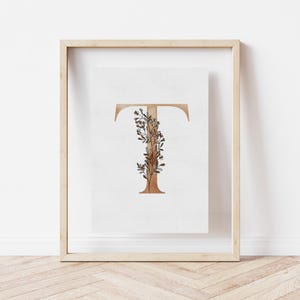 May include: A framed print featuring a watercolour illustration of the letter "T" with a brown and white floral design.
