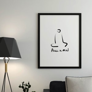 May include: Black and white line art print of a person sitting in a meditative pose with the text "Peace in mind". The print is framed in a black frame and hanging on a white wall.