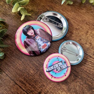 Op de afbeelding: Een verzameling van drie ronde buttons. Eén button toont een persoon in een bruine jas met een kleurrijke achtergrond. Een andere button heeft de tekst "#RUNSEOKJIN EP.TOUR" met muzieknoten. De buttons hebben een metalen speld op de achterkant.
