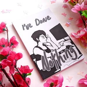May include: A white book with the text "I've Done Nothing" and a black and white illustration of a person at a desk. Pink flowers and butterfly cutouts surround the book.