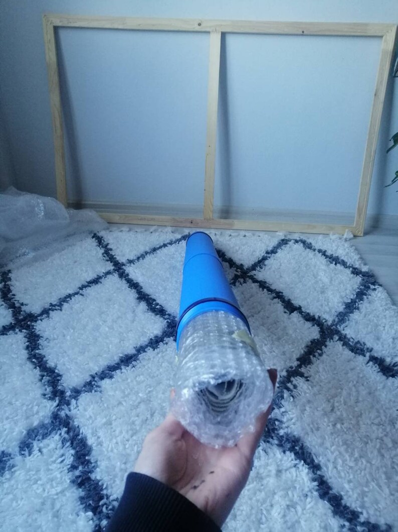 Pu&ograve; includere: Un dipinto su tela arrotolato in un tubo protettivo blu con bolle d'aria. Il tubo &egrave; tenuto da una mano.