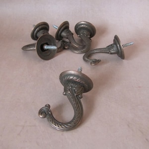 Peut inclure: Ensemble de crochets en métal de couleur bronze antique. Chaque crochet présente un design orné avec une forme incurvée et une vis pour le montage. Idéal pour suspendre des objets.