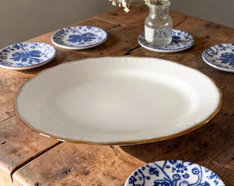 May include: A collection of ceramic tableware on a wooden table. The set includes a large, oval serving platter with a gold rim, and several smaller plates with blue floral patterns. A small glass vase with flowers is also present.