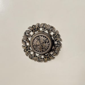 Peut inclure: Bouton de meuble en bronze de style antique avec un motif floral et de feuilles. Le bouton circulaire présente un médaillon central entouré de feuillage détaillé et de petits accents floraux. Le fond est une surface unie, blanc cassé.