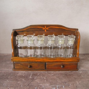May include: A vintage wooden spice rack with six clear glass bottles with glass stoppers. The rack has two small drawers and is painted with orange accents. The rack is made of wood and is designed to hold spices.