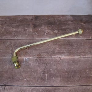 May include: A gold-coloured, curved metal rod with a star-shaped end. The rod has a right-angle bend near the base and a small, rounded fitting. The object is set against a dark wood-grain background.