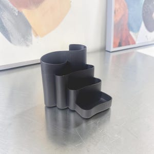 Peut inclure: Un organiseur de bureau noir avec un design unique en gradins. L'organiseur comporte plusieurs compartiments de hauteurs et de profondeurs variables, parfaits pour ranger stylos, crayons et autres fournitures de bureau. Fabriqué en matériau noir mat.