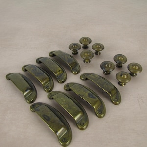 May include: An assortment of antique brass cabinet hardware, including several curved pull handles and round knobs. The hardware has a distressed finish, giving it a vintage appearance. The hardware is designed for furniture.