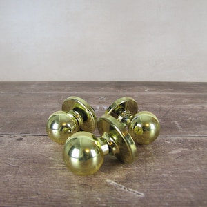 May include: Five polished brass door knobs, each with a spherical handle and a circular base. The knobs are arranged on a wooden surface, reflecting light. These vintage-style knobs would add a touch of elegance to any door.