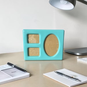 May include: A rectangular turquoise picture frame with a glossy finish. The frame features three distinct openings for photographs: two square-shaped openings on the left side stacked vertically and one large oval-shaped opening on the right side.
