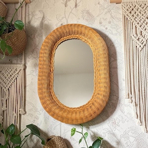 Peut inclure: Un miroir mural de forme ovale doté d'un cadre épais en osier tressé de couleur miel. Le miroir présente une surface en verre lisse et réfléchissante, entourée d'une bordure en osier tressé qui confère un aspect texturé et naturel.