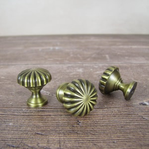 May include: Three antique brass cabinet knobs with a ribbed, pumpkin-like design. The knobs are in various positions, showcasing their detailed construction and aged finish. Ideal for furniture restoration or adding vintage charm.