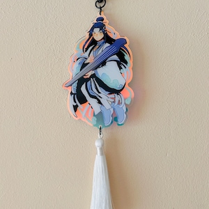 May include: A holographic charm featuring a character with long black hair holding a blue and white instrument. The charm is attached to a white tassel.