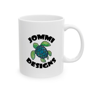 May include: White ceramic mug with a black and green logo that says "JOMMI DESIGNS" and features a blue and green sea turtle.
