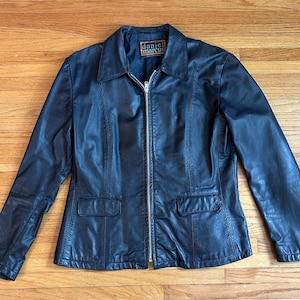 Könnte beinhalten: Schwarze Lederjacke mit Kragen und durchgehendem Reißverschluss. Die Jacke hat zwei Vordertaschen und der Markenname "daniel marcus" ist auf einem Etikett im Kragen zu sehen.