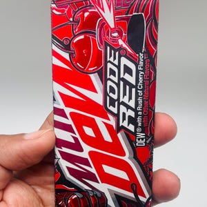 May include: A rectangular Mountain Dew Code Red beverage label featuring a vibrant red, black, and white graphic design. The label displays the text Code Red with a Rush of Cherry Flavor and Dew with Other Natural Flavors, alongside cherry illustrations.