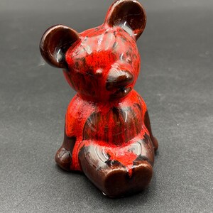 Peut inclure: Figurine d'ours en céramique en position assise. L'ours est principalement rouge avec des détails marron foncé, créant un contraste saisissant. La finition brillante rehausse les couleurs. Cet objet décoratif pourrait être un objet de collection ou une pièce de décoration intérieure unique.