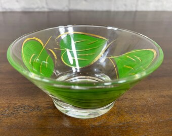 May include: A small, clear glass bowl with a green and gold leaf design. The bowl is perfect for serving snacks or dips.