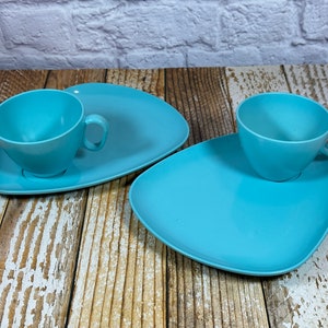 May include: Two light blue plastic plates with matching light blue plastic cups. The plates are shaped like a triangle with rounded corners. The cups are round with a handle.