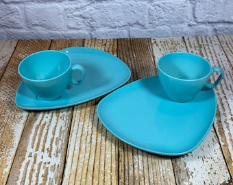 May include: Two light blue plastic plates with matching light blue plastic cups. The plates are shaped like a triangle with rounded corners. The cups are round with a handle.