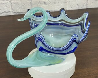 May include: A blue and white glass swan shaped bowl with a wavy design. The bowl is on a white pedestal.