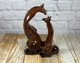 May include: A brown ceramic sculpture of two giraffes intertwined, with one giraffe's neck curved around the other's body.