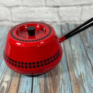 May include: Red fondue pot with a black handle and a black and white geometric design. The pot has a lid with a black knob.