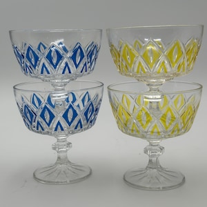 Puede incluir: Cuatro copas de postre de vidrio transparente con un patrón geométrico. Dos copas tienen un patrón azul y dos copas tienen un patrón amarillo.