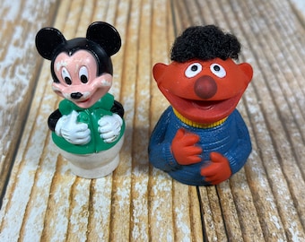 May include: A vintage Mickey Mouse and Elmo finger puppet set. Mickey Mouse is wearing a green shirt and white pants. Elmo is wearing a blue sweater.