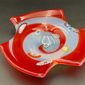 May include: A decorative glass dish with a red and pale blue spiral design. The dish has a unique shape with curved edges and is adorned with colourful floral accents. This art glass piece is a vibrant addition to any home decor.