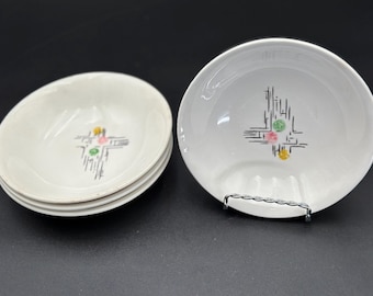 May include: Set of four white ceramic bowls with a mid-century modern design. Each bowl features a black geometric pattern with yellow, pink, and green accents. The bowls are displayed on a dark surface.