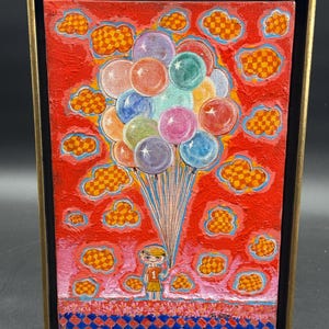 May include: A framed painting on canvas depicting a person wearing an orange shirt with the number 1, holding a large bunch of colorful balloons against a bright red background filled with orange and yellow checkered clouds and a blue checkered border.