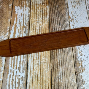 Peut inclure: Un plateau de service rectangulaire en bois long avec un bord surélevé. Le plateau est en bois brun foncé et a une finition lisse et polie.