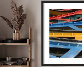 May include: A framed photograph of a stack of colorful wooden boats. The boats are painted in shades of blue, yellow, red, and green. The boats are weathered and have a rustic look.