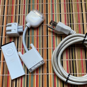May include: A set of white Apple accessories for an Apple TV, including a remote control, a power adapter, and two white cables with connectors.
