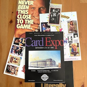 May include: A collection of vintage sports memorabilia, including a "Card Expo" flyer from 1992, a promotional poster with a man's face, and various trading cards. The items are arranged on a wooden surface.