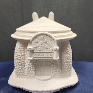 May include: White ceramic figurine of a small stone building with a rounded roof, a sign that reads "PIZZERIA", and a round window with a pizza design.