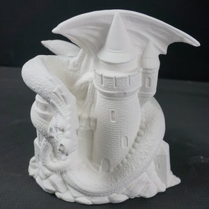 May include: White ceramic figurine of a dragon wrapping around a tower. The dragon has wings and a detailed, textured body. The tower has a pointed roof and windows.