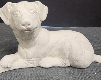 May include: A white ceramic figurine of a dog lying down. The dog has a sweet expression and is sculpted in a realistic style.