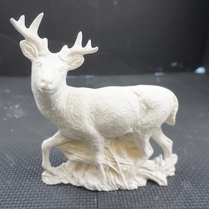 May include: White ceramic deer figurine standing on a base with a textured surface. The deer has a detailed face and antlers.