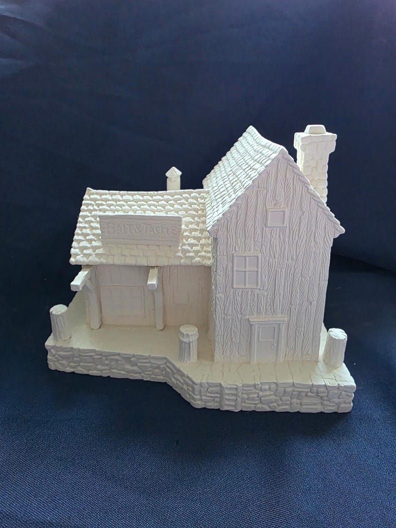May include: A detailed, off-white miniature Bait & Tackle shop. The model features a textured roof, siding, and chimney. The shop has a small door, windows, and a sign that reads "Bait & Tackle". The base is made to look like stone.